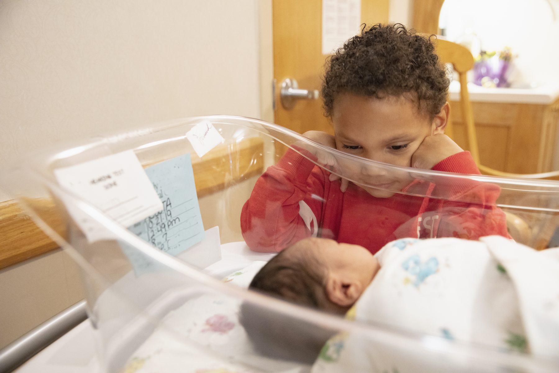 A child looking at their newborn sibling in a hospital bassinet